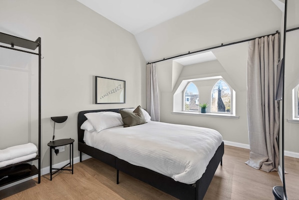 A modern bedroom with a bed, a bedside table, a floor lamp, and a window with curtains.