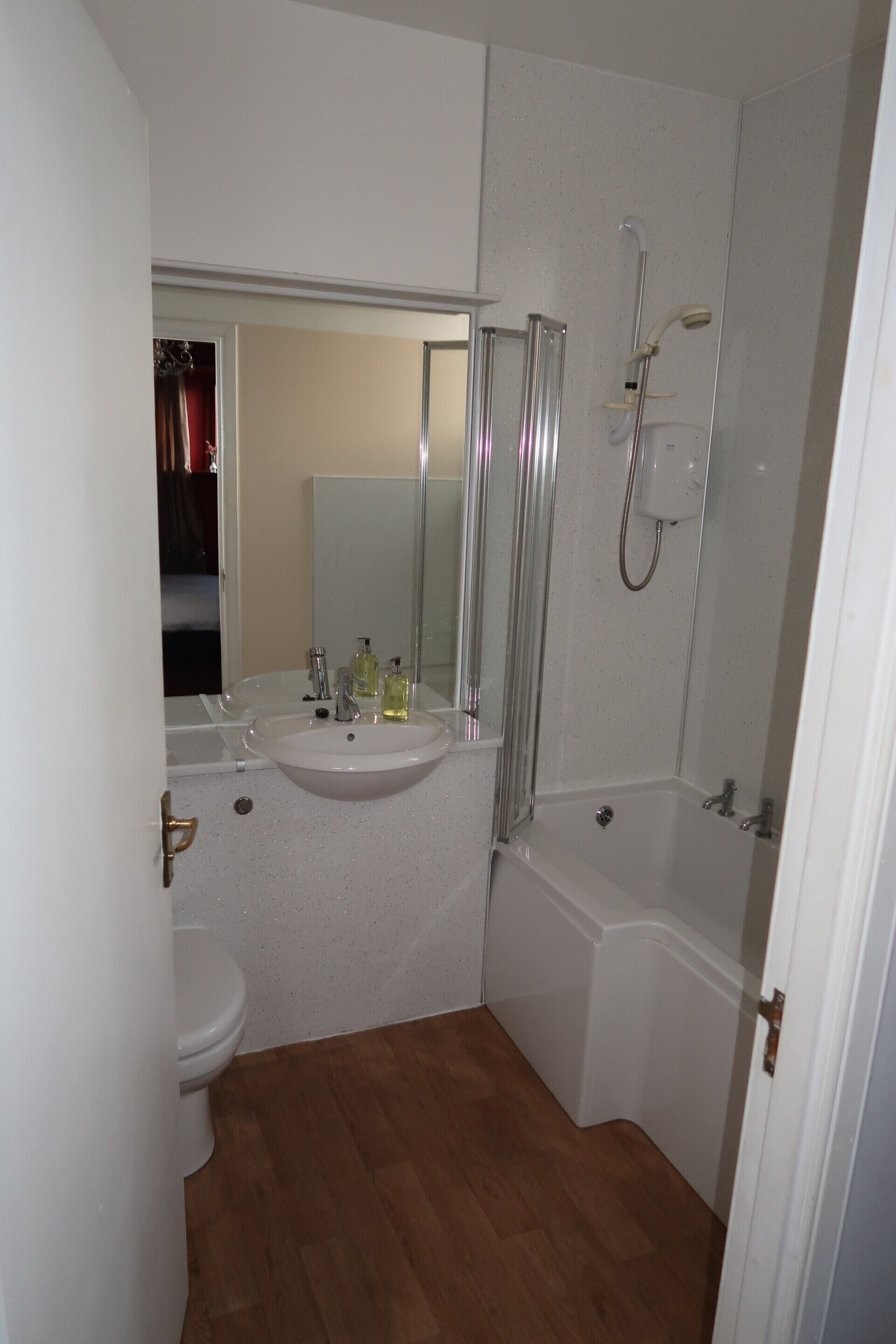 A compact bathroom with a sink, mirror, toilet, and shower.