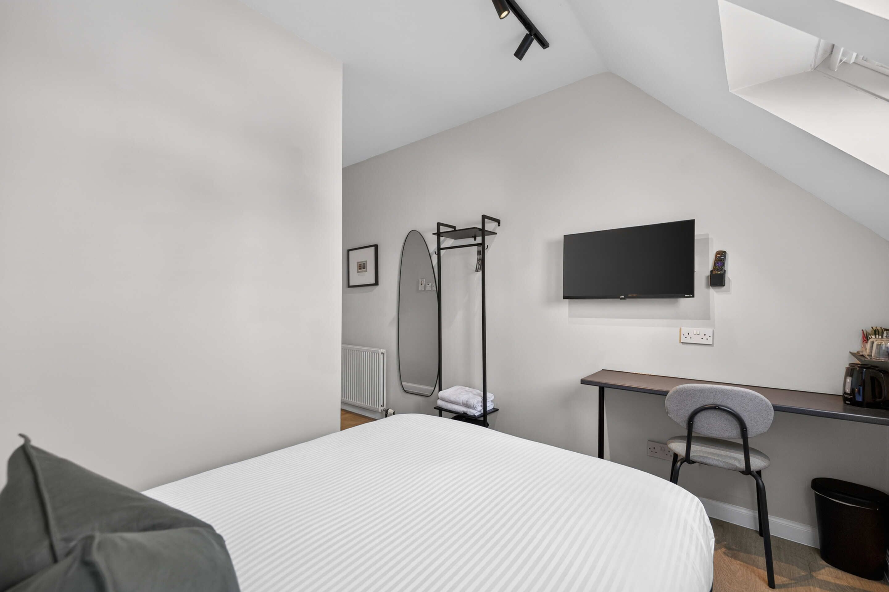 A modern, minimalistic bedroom with a bed, a desk, a chair, and a TV.