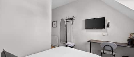 A modern, minimalistic bedroom with a bed, a desk, a chair, and a TV.