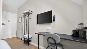 Habitación de hotel con cama, escritorio, silla, televisor, radiador y estante con toallas.