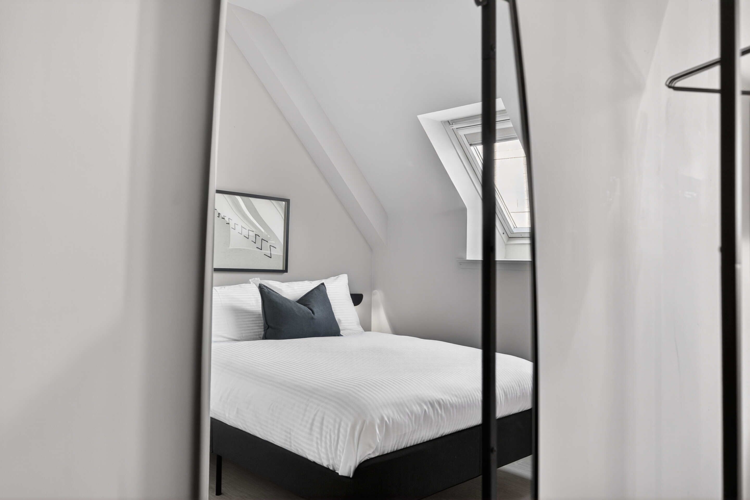 Ein modernes Schlafzimmer mit einem Bett, einem gerahmten Bild an der Wand und einem Dachfenster.