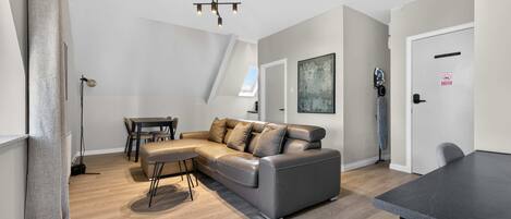 A modern living room with a sectional sofa, a dining table, and a ceiling light fixture.