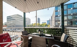 A balcony with wicker furniture, a table set for dining, and a view of city buildings. - Luxury Duo Suites - King Bed - AC - Patio - UGPark (Edmonton)