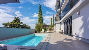 A swimming pool with lounge chairs, a pergola, and tall trees. - Modern vacation apartment with pool and sea view (Crikvenica)