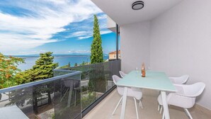 A balcony with a table and chairs, a bottle, and a view of the sea and trees. - Modern vacation apartment with pool and sea view (Crikvenica)