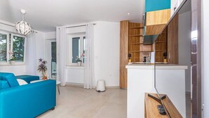 A modern living room with a blue sofa, a small table with a vase, and a kitchen area with wooden cabinets and a countertop. - Modern vacation apartment with pool and sea view (Crikvenica)