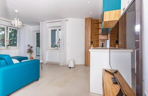 Ein modernes Wohnzimmer mit einem blauen Sofa, einem kleinen Tisch mit einer Vase und einer Küchenzeile mit Holzschränken und einer Arbeitsplatte.