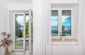 Ein Zimmer mit einer Schiebetür zum Balkon, einer Orchidee im Topf auf der Fensterbank und Blick auf ein Gewässer und Bäume.