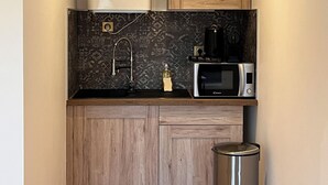 Una cocina compacta equipada con calentador de agua, microondas, cafetera y un cubo de basura.