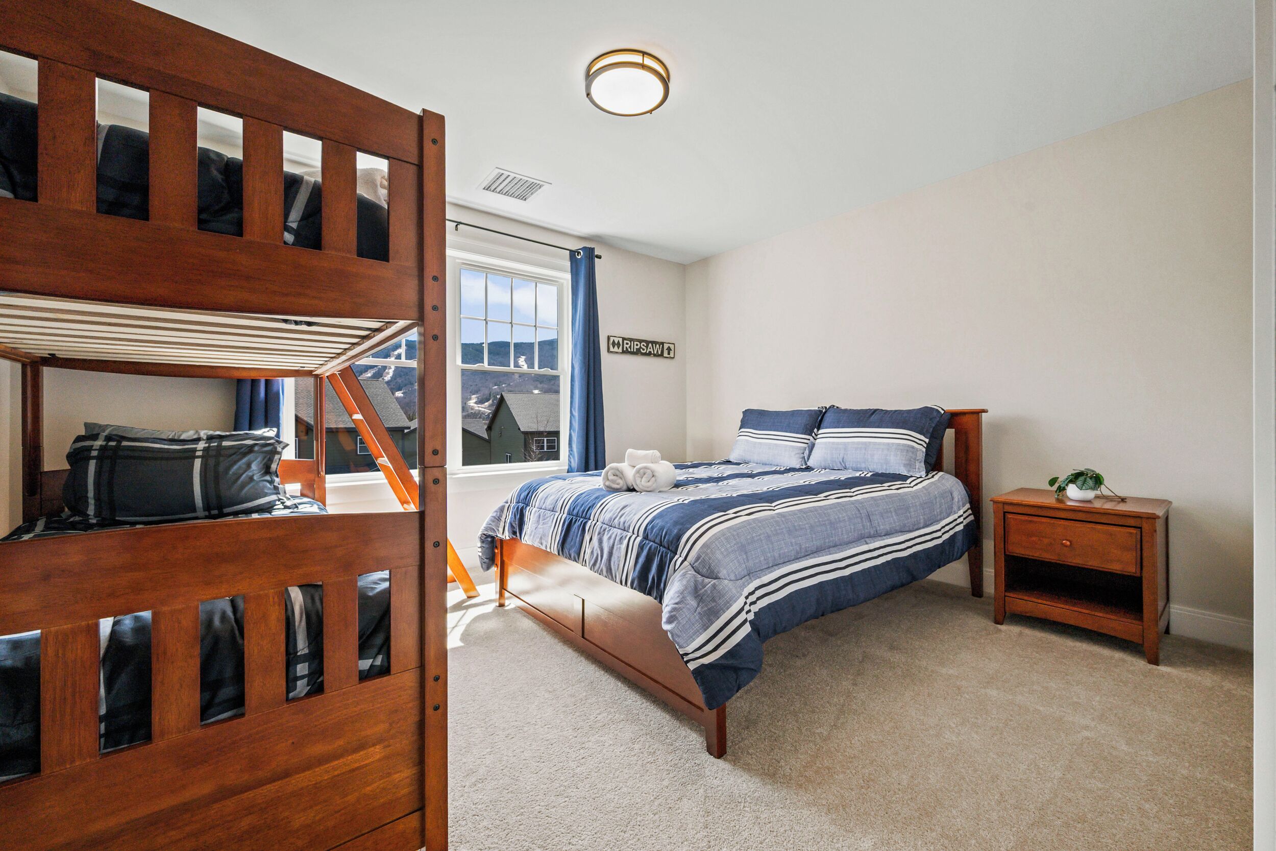 A bedroom with a bunk bed, a single bed with striped bedding, a nightstand with a plant, and a window with a view.
