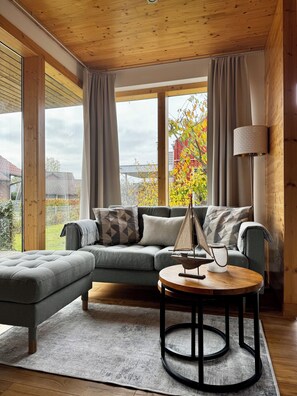 Ein modernes Wohnzimmer mit einem grauen Sofa, einem runden Holztisch und einer Lampe.