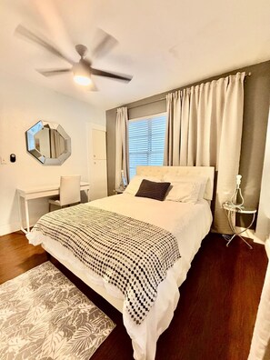 A bedroom with a bed, a desk, a chair, a ceiling fan, a window with curtains, and a mirror on the wall. - 1 BR on Collins Ave. steps away from the BEACH (Miami)