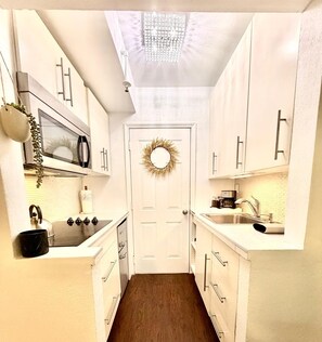 A narrow kitchen with white cabinets, a microwave, a sink, and a ceiling light fixture. - 1 BR on Collins Ave. steps away from the BEACH (Miami)