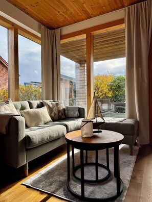 Ein modernes Wohnzimmer mit einer Eckcouch, einem runden Couchtisch und großen Fenstern mit Blick nach draußen.