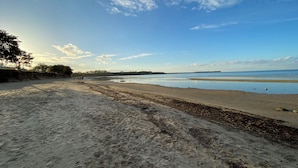 Een strand met een zandrijk strand, kalm water en een heldere lucht met wolken.