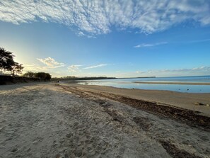 Ein Strand mit sandigem Ufer, ruhigem Wasser und einem klaren Himmel mit Wolken.