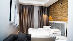 Una habitación de hotel moderna con una cama, cortinas grises, un sofá gris y una pared decorativa de madera.