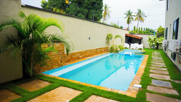 Una piscina con borde de piedra, rodeada por un césped cuidado y palmeras.