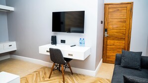 Una habitación moderna con un escritorio blanco, televisor montado, puerta de madera y sofá gris.