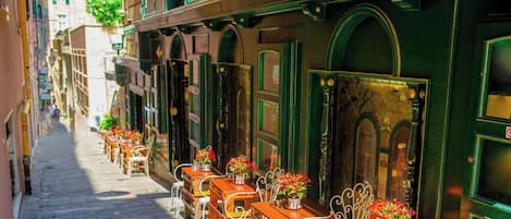 A narrow street with outdoor seating and green awnings.
