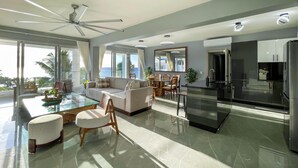 A modern living room with a glass dining table, a sofa, and a kitchen area with a refrigerator. - Romantic, Oceanfront Getaway! (Sosúa)