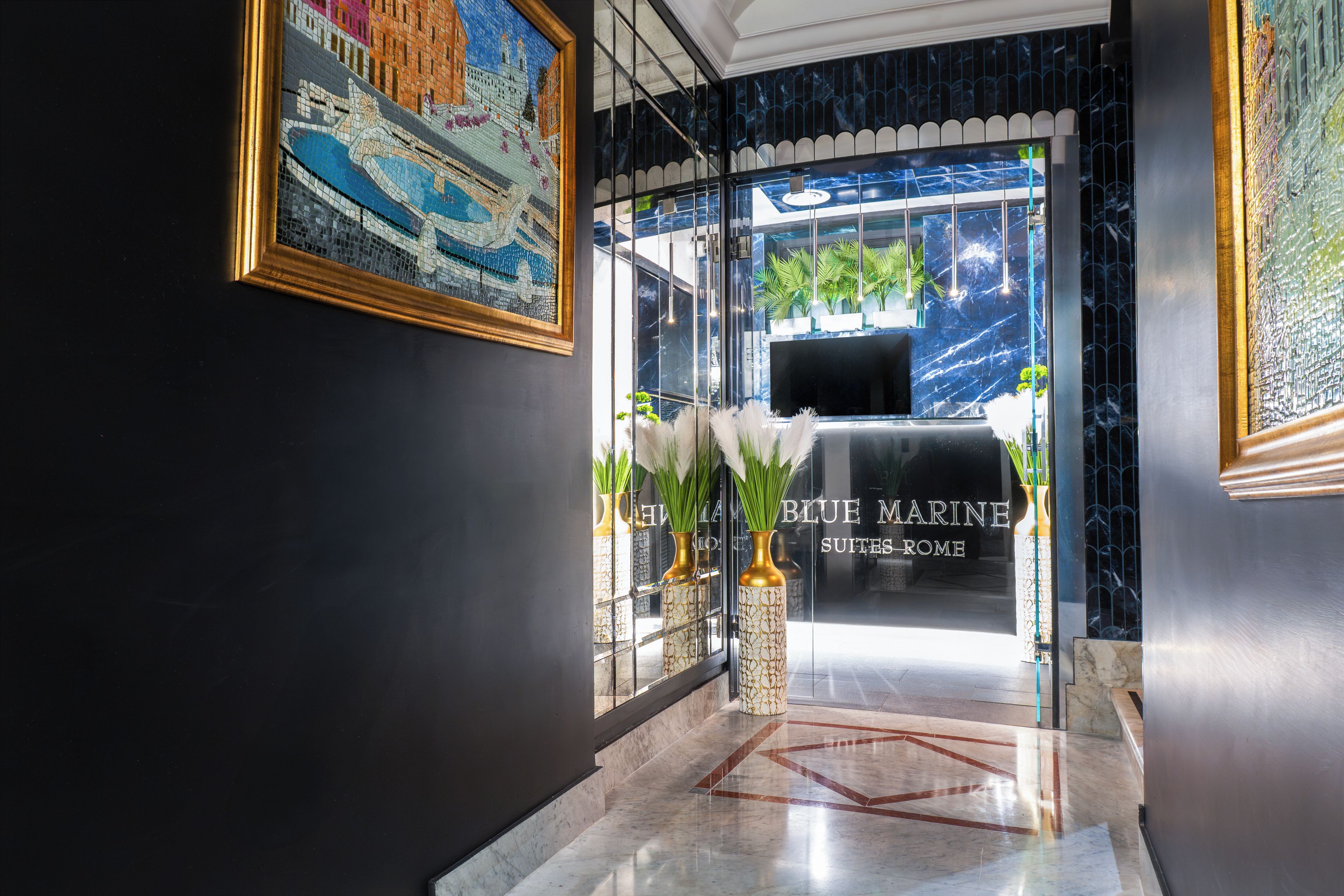 Un vestíbulo de hotel con una recepción, una obra de arte en mosaico y un suelo de mármol.