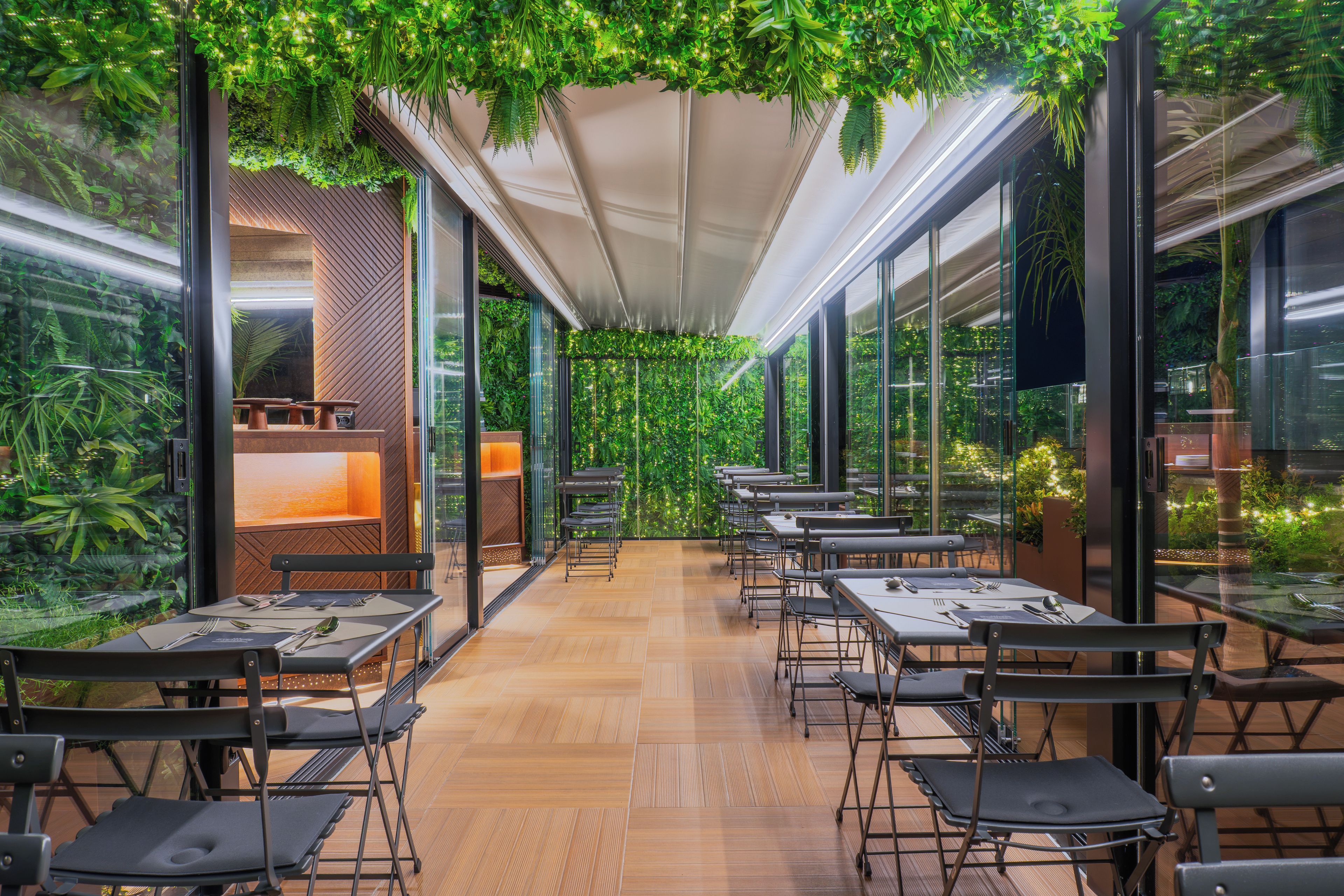 A restaurant with a long table layout, glass walls, and indoor plants.