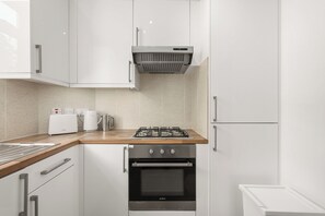 Una cocina moderna con armarios blancos, una campana extractora de acero inoxidable, horno integrado y encimera de madera.