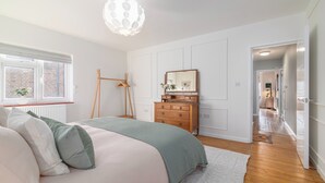 Ein Schlafzimmer mit Bett, Kommode, Spiegel und einem Flur, der in einen weiteren Raum führt.