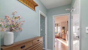 Ein Flur mit einem Holzkonsolenmöbel, einem Blumenstrauß, einer gemusterten Wand und einer offenen Tür zu einem anderen Zimmer.