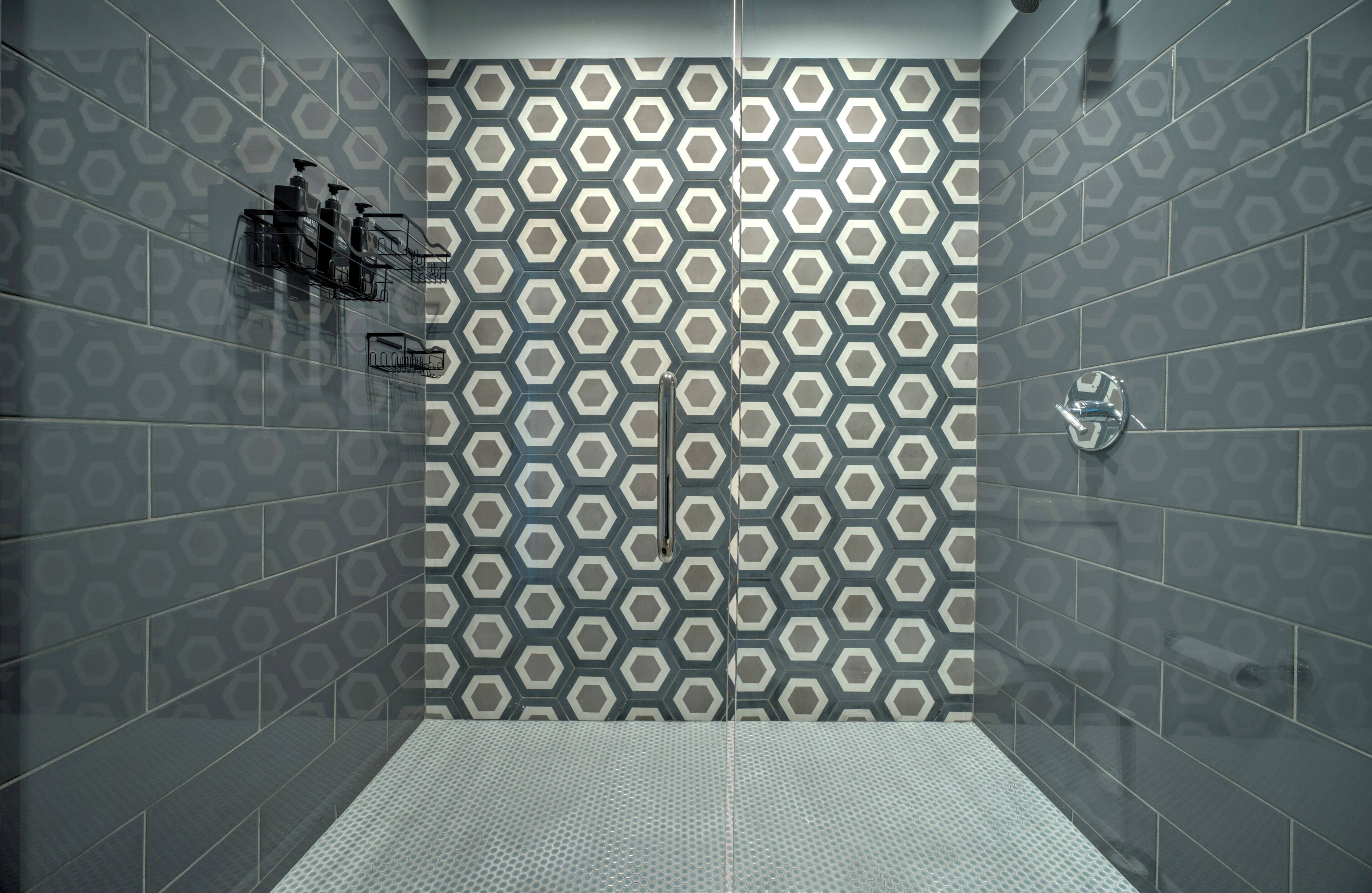 Een douche met een geometrisch tegelpatroon, een metalen douchekop en een metalen plank met toiletartikelen.