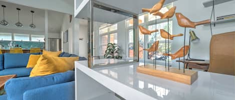 Ein modernes Wohnzimmer mit einem blauen Sofa, gelben Kissen, einem Glastisch und Holzskulpturen von Vögeln.