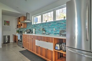 A modern kitchen with wooden cabinets, a stainless steel refrigerator, and a blue-tiled backsplash. - Modern Designer Retreat (Chattanooga)