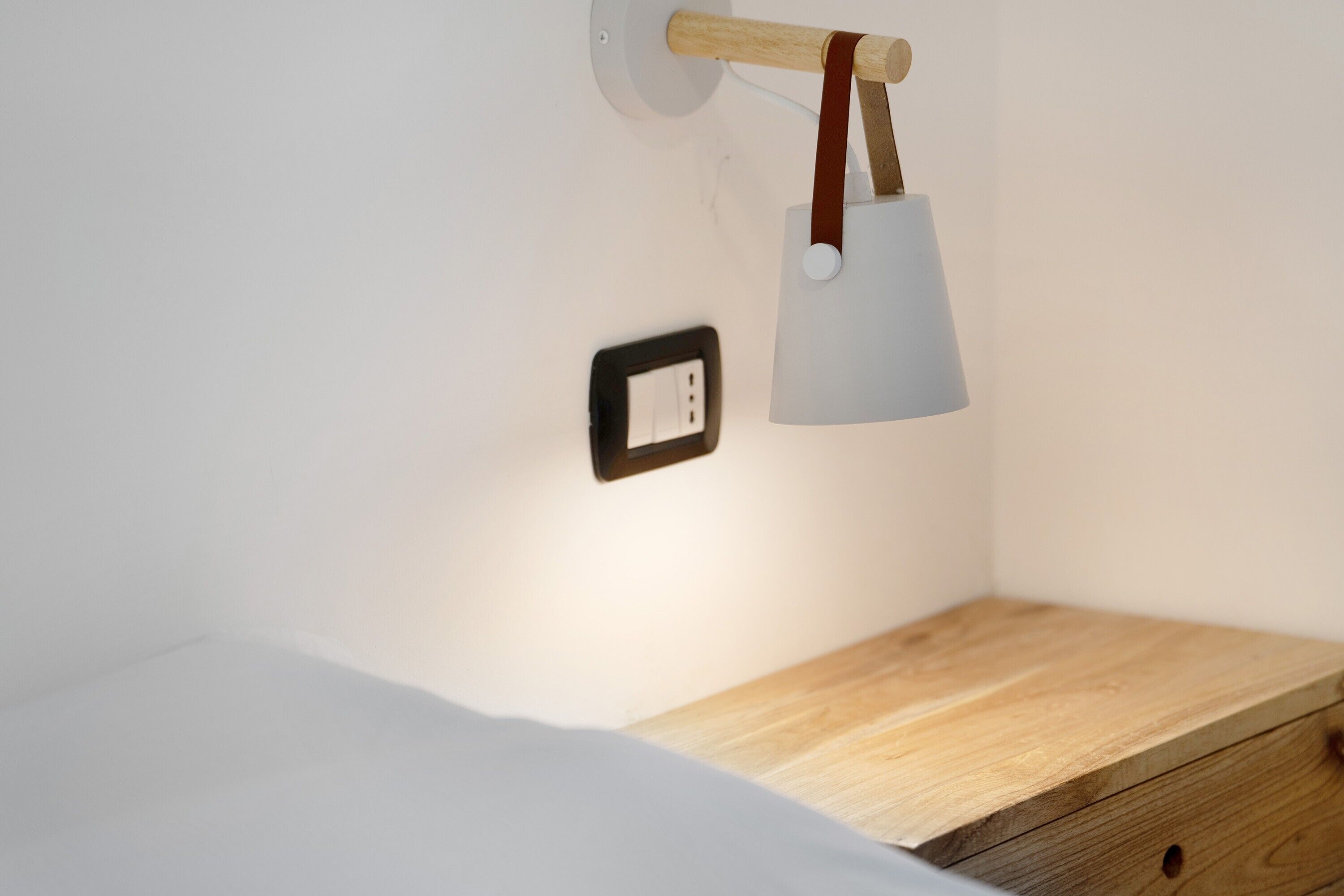 A bedside table with a lamp, a power outlet, and a wooden nightstand.
