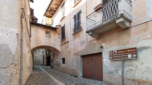A narrow cobblestone street with buildings on either side, a signpost with directions, and an arched doorway. - Relax and Recharge in This Refined Oasis of Tranquility (Miasino)