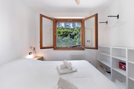 A bedroom with a bed, a window, a radiator, and a shelf with a box.. Relax and Recharge in This Refined Oasis of Tranquility