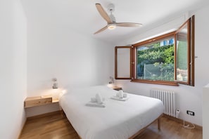 Een slaapkamer met een bed, een plafondventilator, een raam met uitzicht, een nachtkastje en een bedtafel.