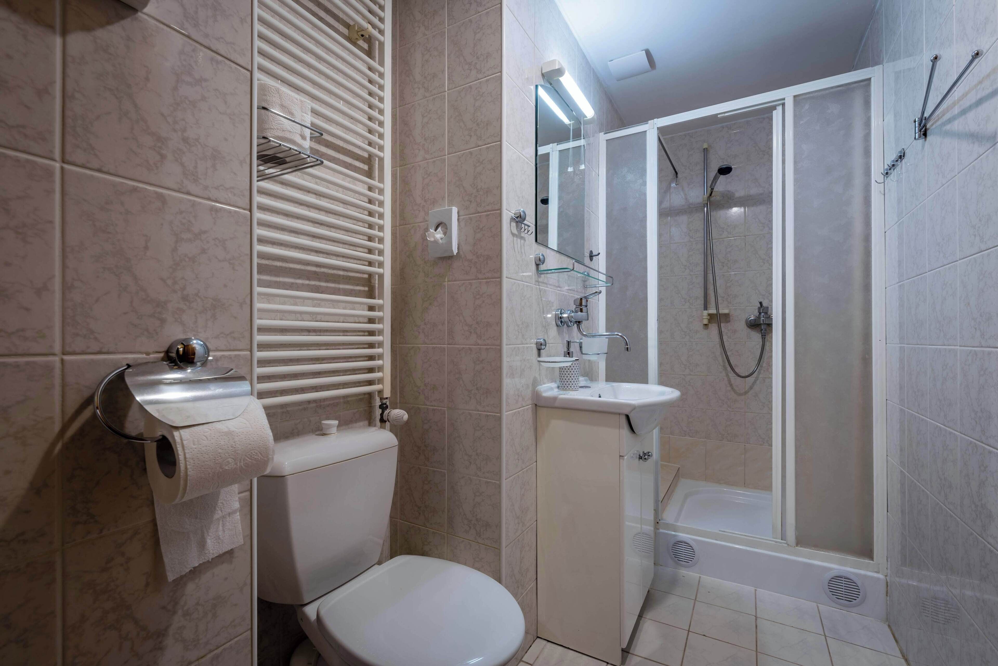 A bathroom with a toilet, a glass shower enclosure, a sink, and a towel rack.