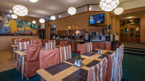 A hotel dining area with striped chairs, a long table, and hanging pendant lights.