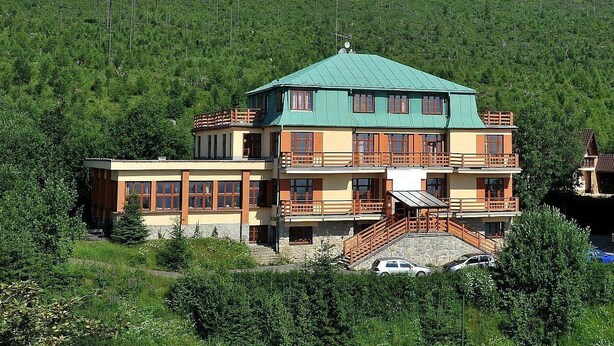 A multi-story building with balconies, set against a mountainous backdrop.