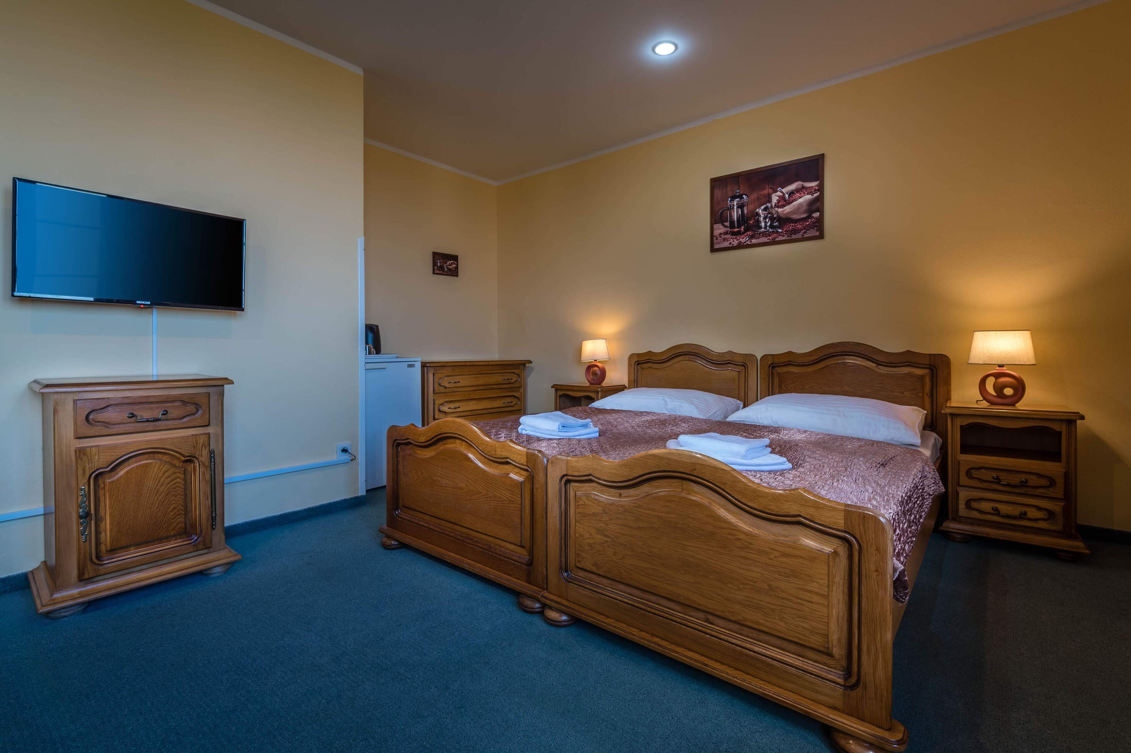 Une chambre d’hôtel avec un lit en bois, des lampes de chevet, un téléviseur à écran plat, un petit meuble et un tableau au mur.