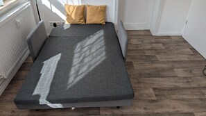 Ein Bett mit grauem Matratze, zwei gelben Kissen und Holzboden.