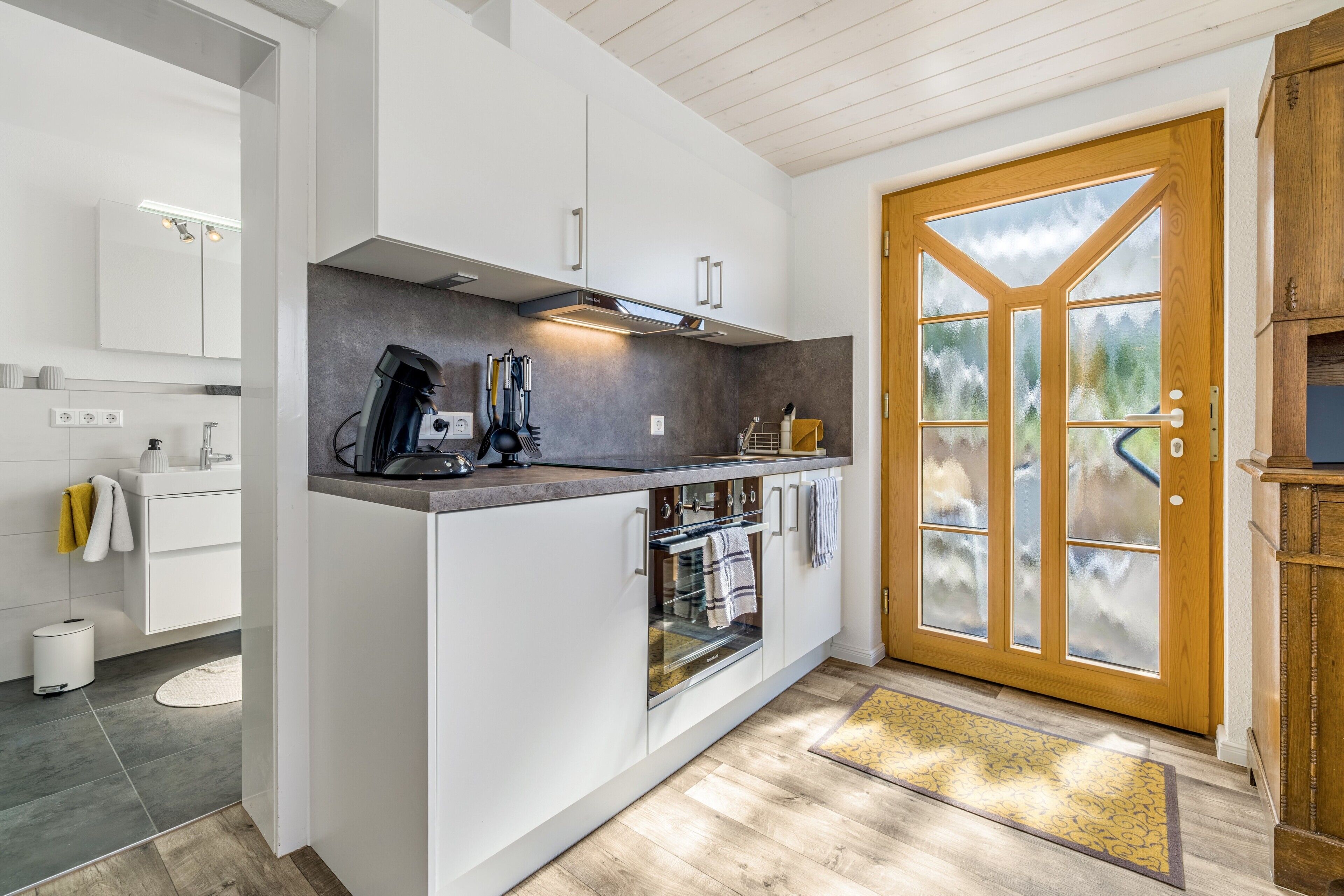 A modern kitchen with white cabinetry, a built-in oven, and a large window with frosted glass panels.