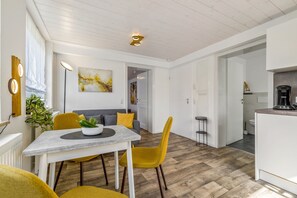 Una cocina moderna con cafetera, un comedor con mesa y sillas, y una sala de estar con sofá y cojines.
