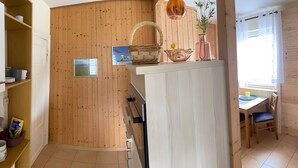 Eine Küche mit Holzwänden, einer weißen Arbeitsplatte, einem Korbwäschesammler, einer Vase mit Blumen und einem Fenster mit Vorhängen.