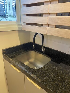 Eine Küche mit Spüle aus Edelstahl, schwarzer Granitabdeckung und Holzschränken.