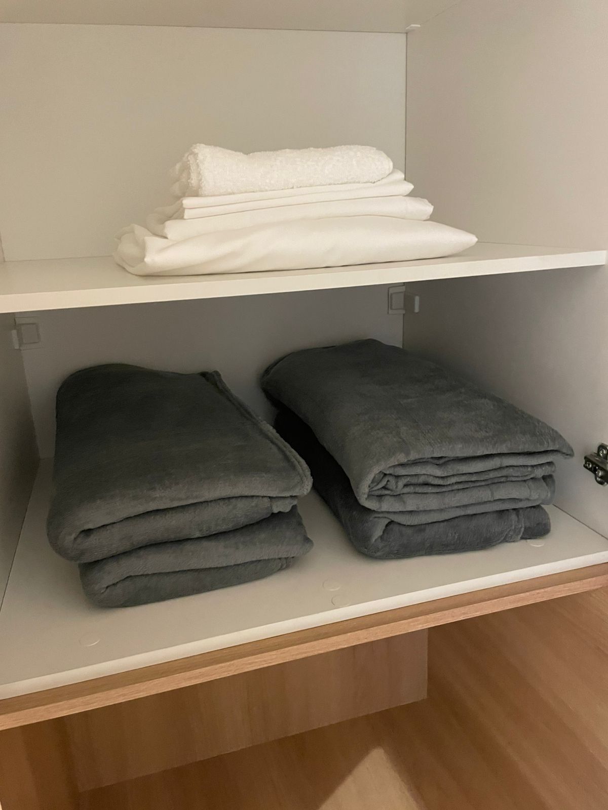 A storage area with two shelves, one holding folded white towels and the other holding folded gray towels.