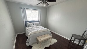 A bedroom with a bed, a chair, a ceiling fan, and a window with curtains. - Apartment near Hobby Airport (Houston)