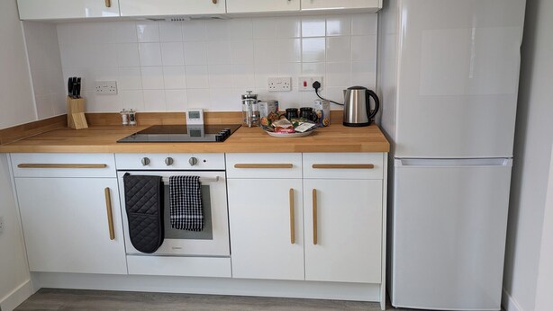 Una cocina con armarios blancos, un refrigerador de acero inoxidable, una encimera de madera y un horno empotrado.